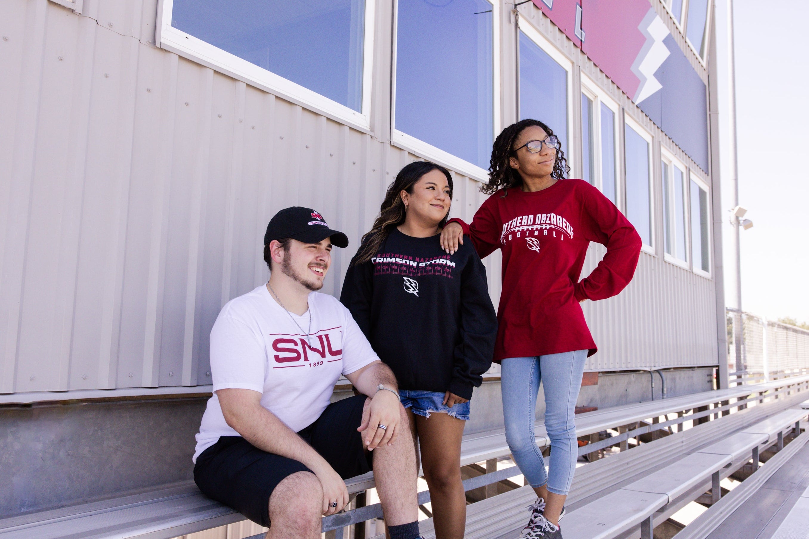 Three people wearing college apparel on stadium stands