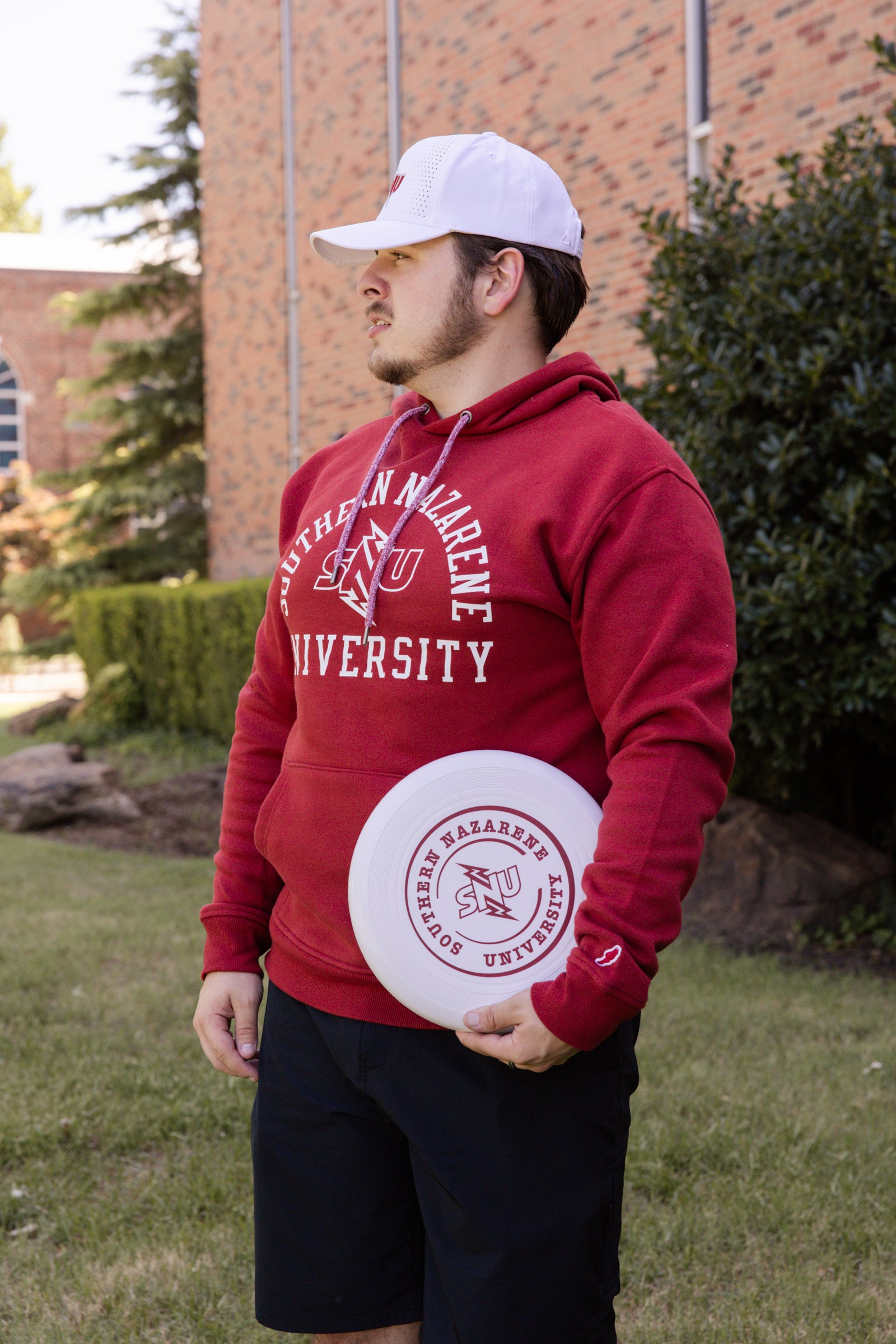 Person wearing a red hoodie holding a white frisbee with university logo.
