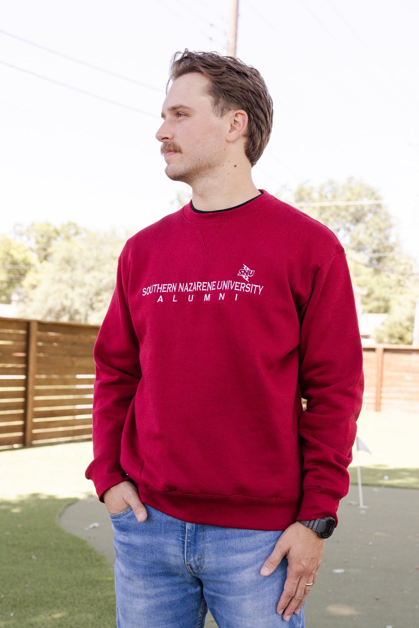 Man wearing a red Southern Nazarene University Alumni sweatshirt outdoors.