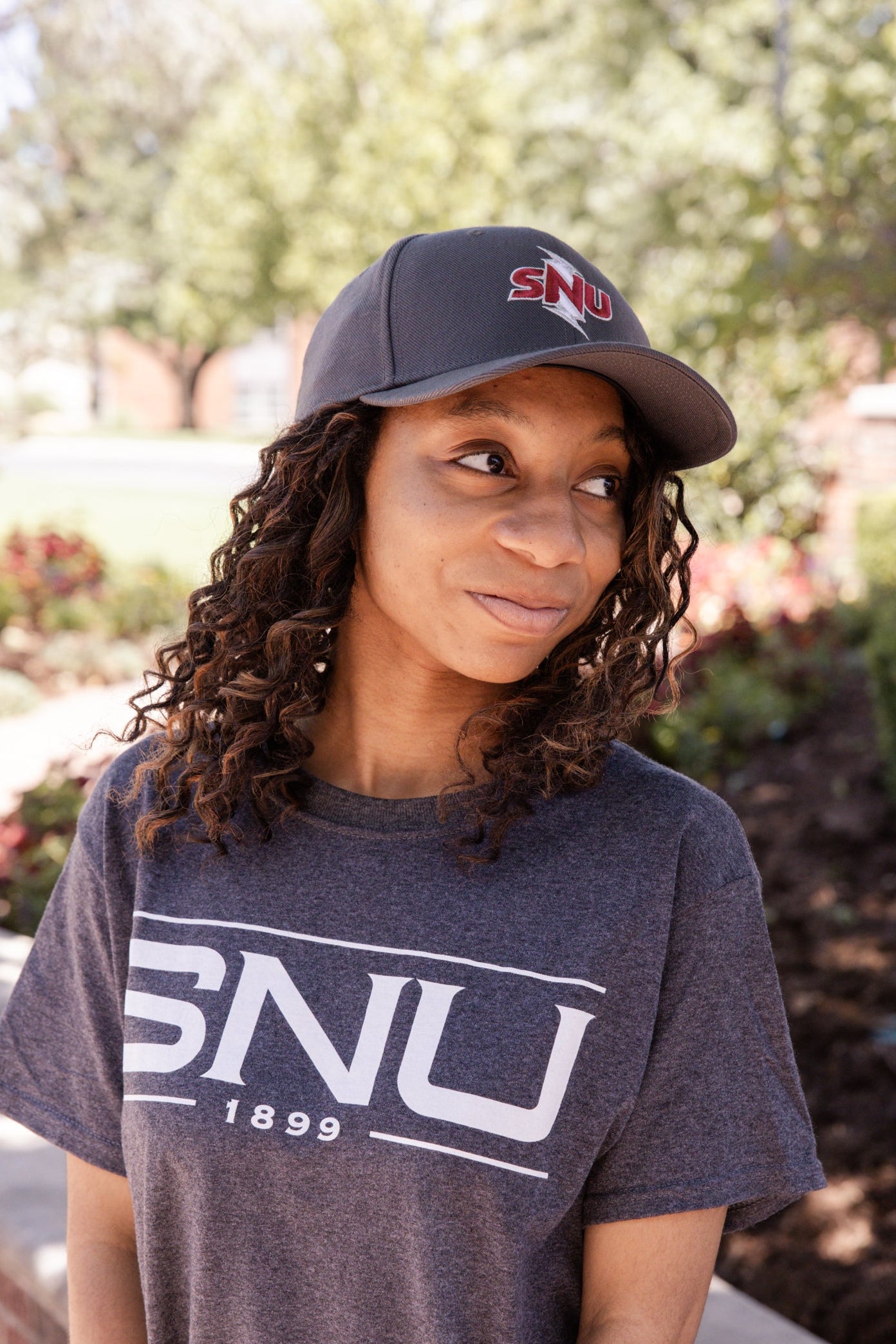 Person wearing a cap and t-shirt with 'SNU' branding standing outdoors